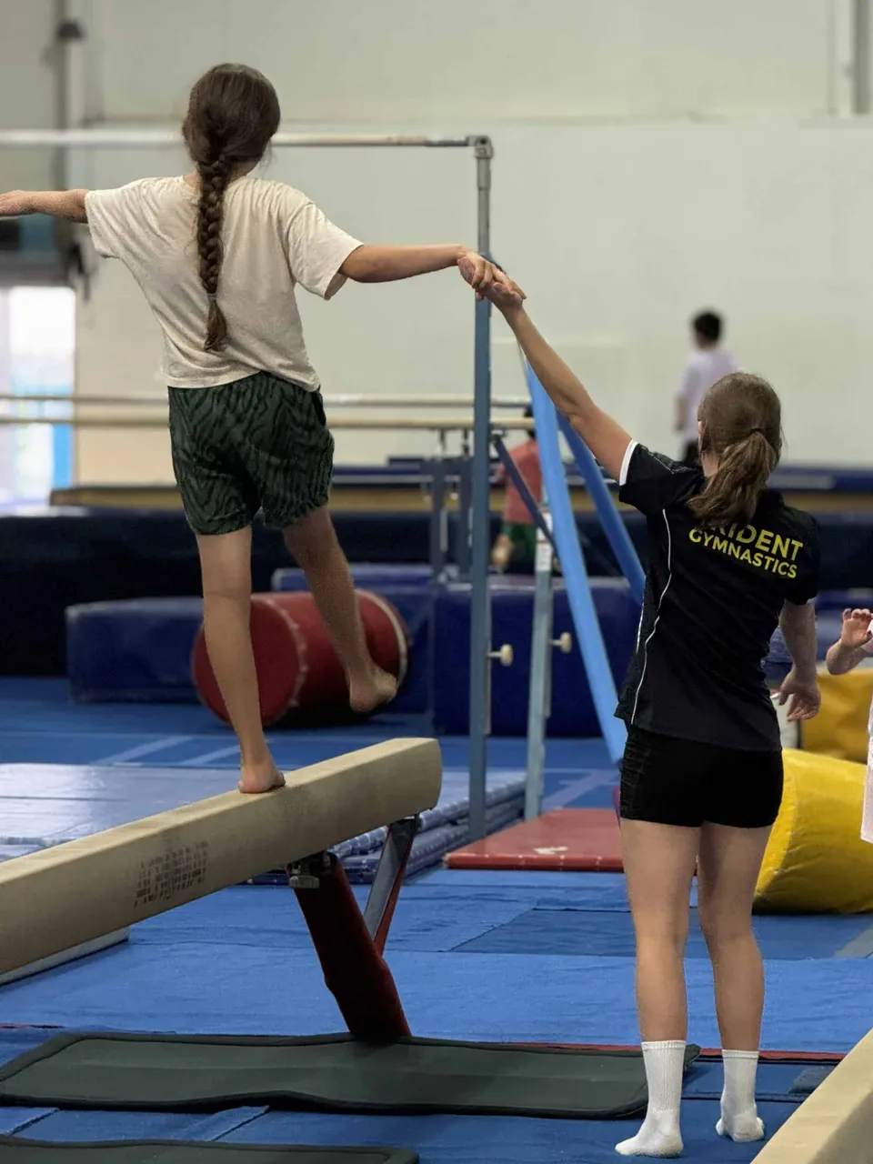 A Trident coach spotting a student as they walk along the balance beam