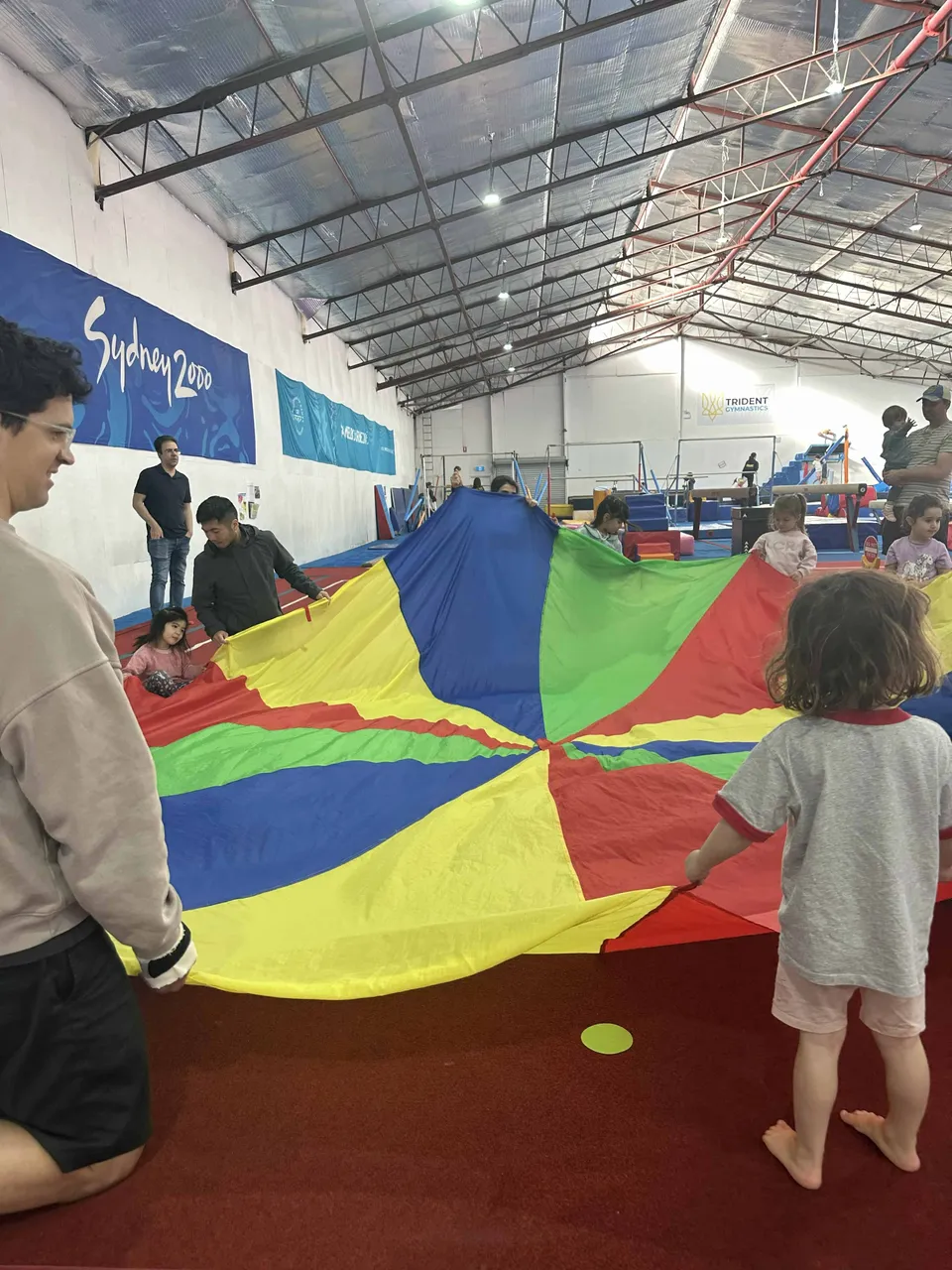 Children and coaches playing together under a rainbow parachute