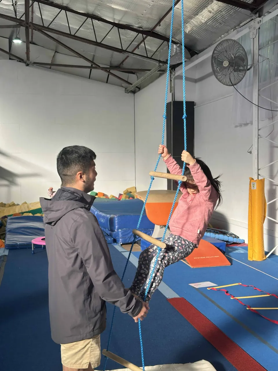 A coach supporting a young child climbing on a rope ladder