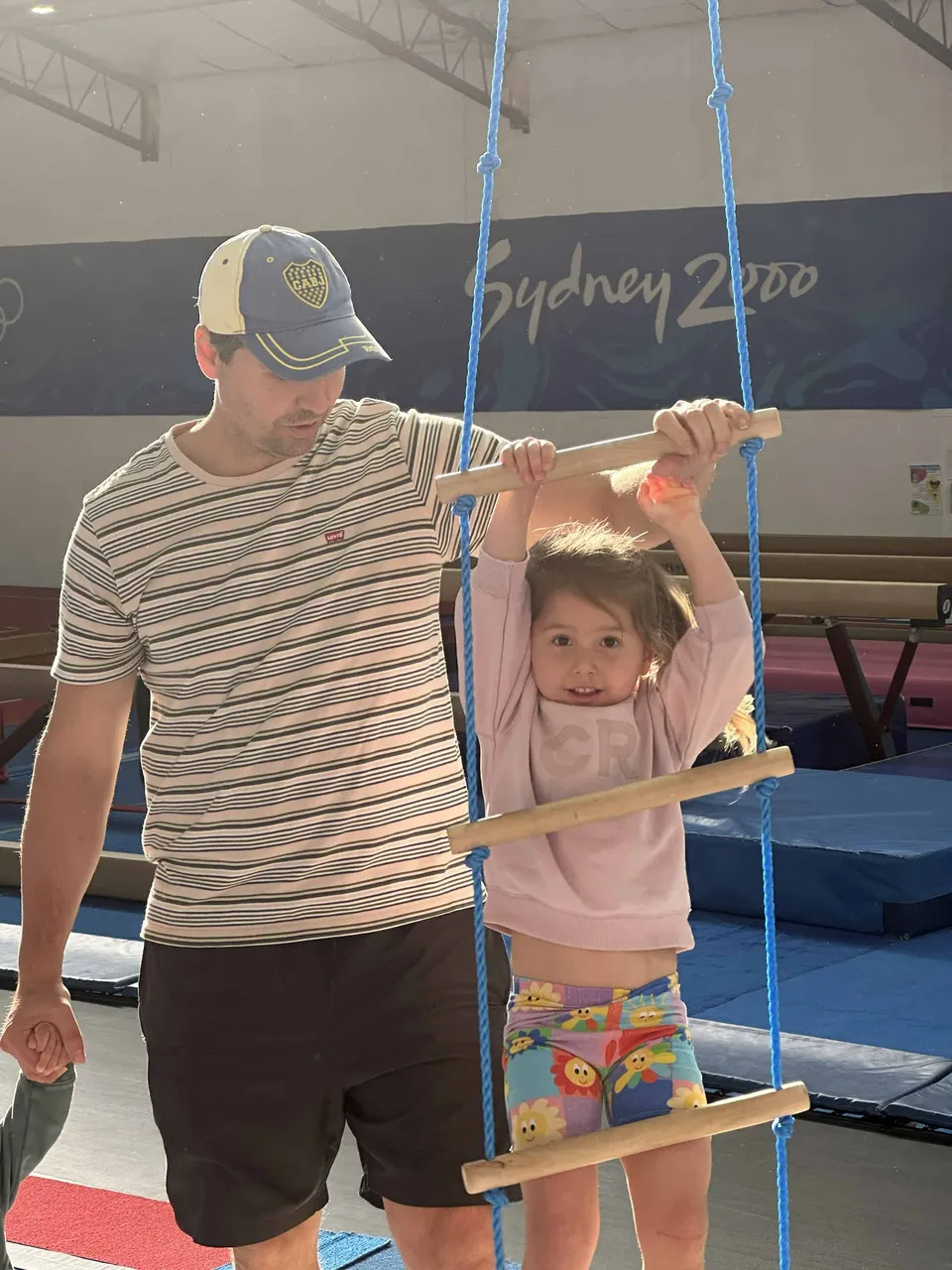 A parent helping their toddler hold onto a trapeze bar